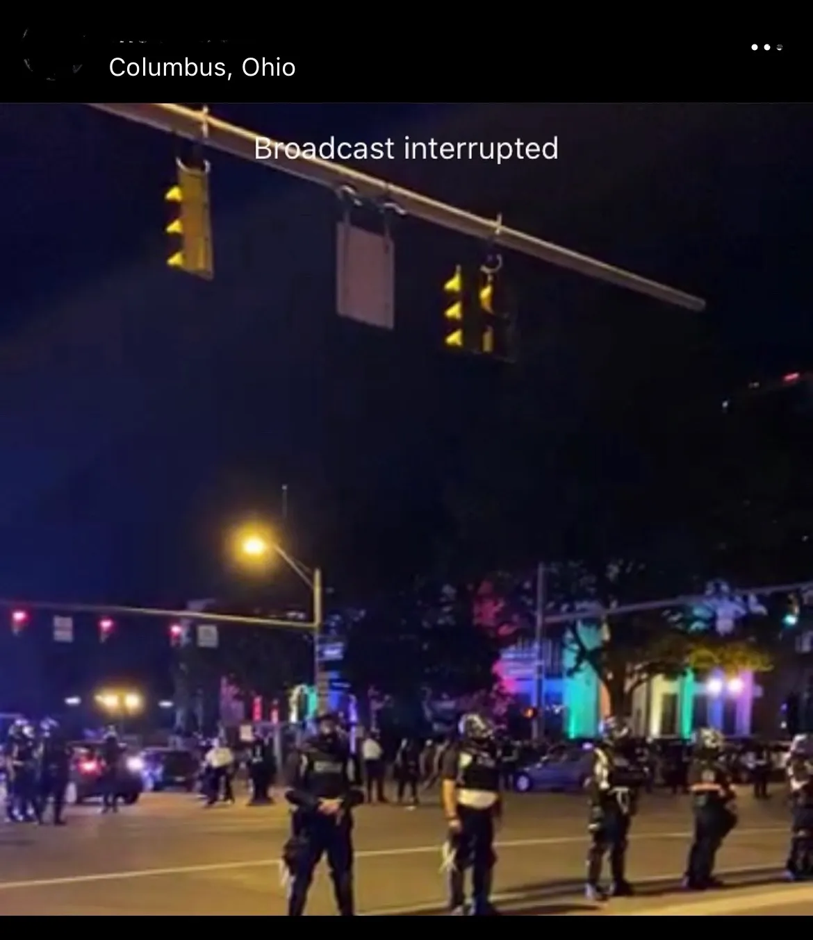 a screenshot from June 24, 2020, shows CPD in riot gear and in formation in front of the Ohio Statehouse, lit up in rainbow colors for Pride Month. Text at the top of the photo reads: broadcast interrupted.