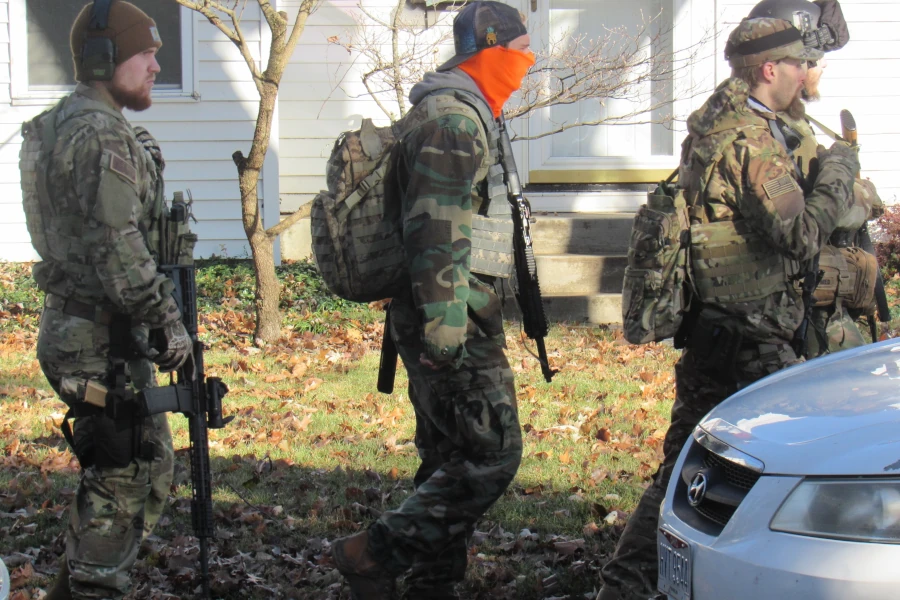 three white men in fatigues with long guns walk down a residential street in front of a house in Clintonville, Columbus, OH. 12/3/2022.