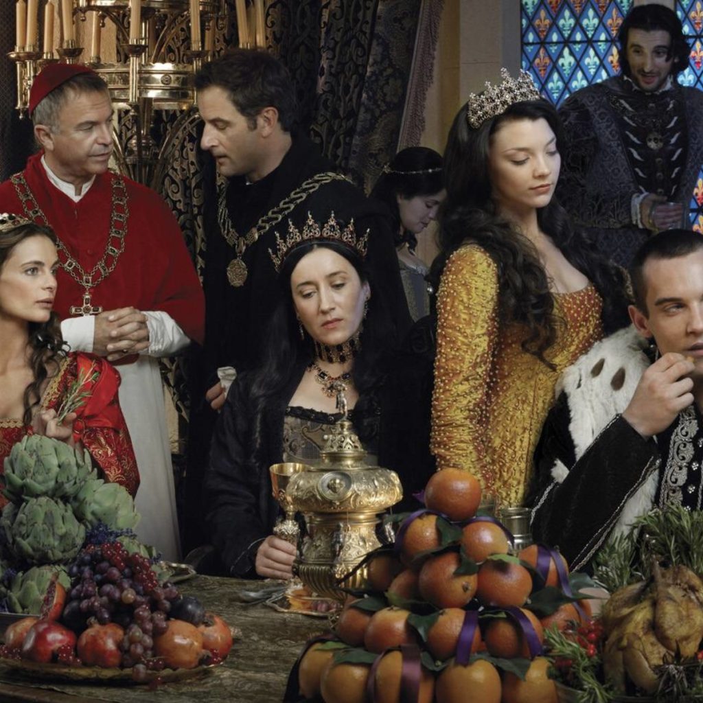 Image of the cast in costume from Showtime's series The Tudors. Left to right are Gabrielle Anwar as Margaret Tudor; Sam Neill as Bishop Thomas Wolsey in a red cap and red robe; Jeremy Northam as Sir Thomas More in black, standing next to the Bishop. Seated before him in black wearing a crown is Maria Doyle Kennedy playing the role of Katherine of Aragon, Queen of England and Catholic daughter of the Queen of Castille and King of Aragon; beside her standing in gold wearing a crown is Natalie Dormer as Lady Anne Boelyn, Mistress to King Henry VIII and Queen of England; next to her on the right of the image, seated, is Jonathan Rhys Meyers, playing King Henry VIII, King of England