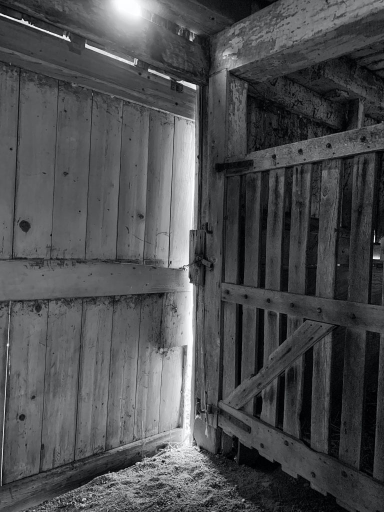 black and white image of a barn door slightly open, allowing a crack of light in