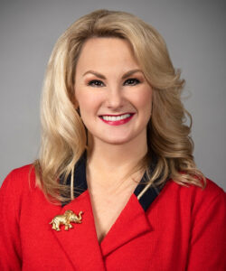 Image of Melanie Miller from her profile in the Ladies Gallery on the Ohio dot gov website. She's a white woman with bright red lipstick, shoulder length blonde hair, wearing a red top with collar and gold elephant pin